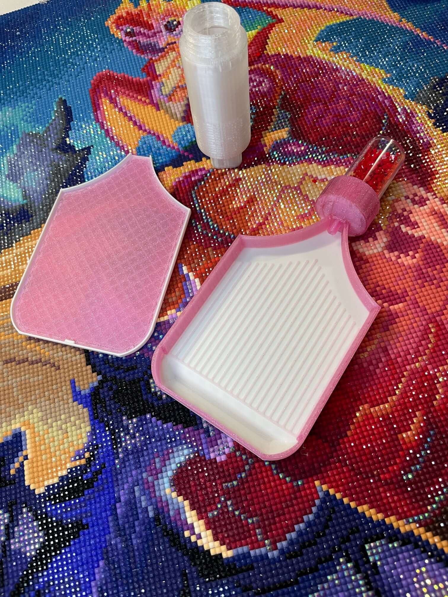 Pink and white Dragonling Screw & Shake diamond art trays with white base on colorful background.